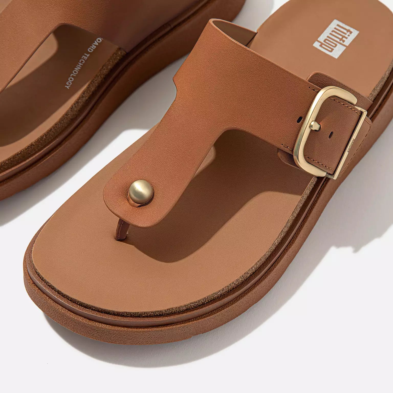 Ergonomic HE7 592 Light Tan FitFlop sandals with brushed-metal buckle, domed stud, natural arch support, and lightweight cork-mix sole for everyday wear.