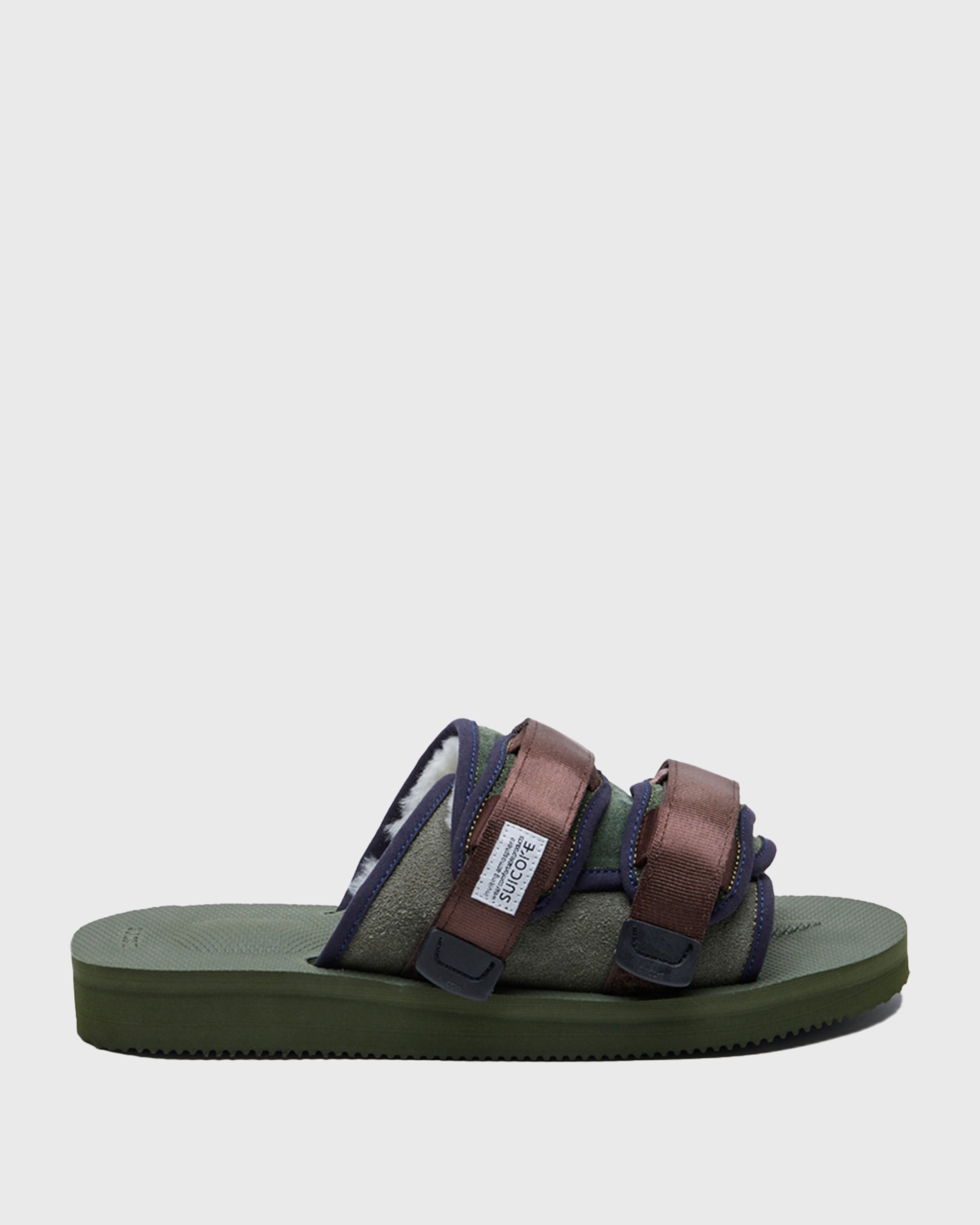 SUICOKE MOTO-Mab suede slides with green midsole and sole, green suede upper and shearling inside with navy piping and brown nylon straps with a logo patch. From Fall/Winter 2021 collection on SUICOKE Official US & Canada Webstore.