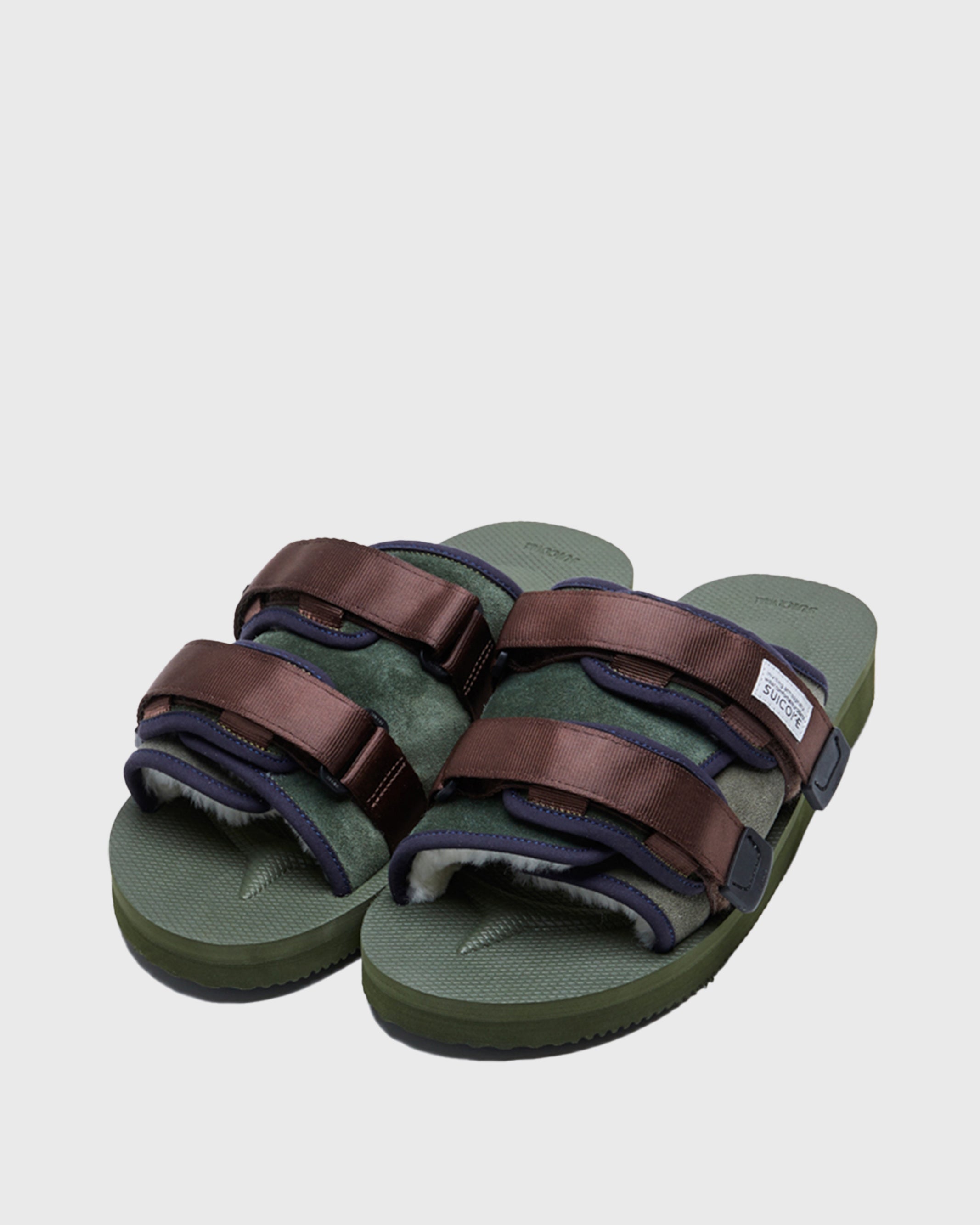 SUICOKE MOTO-Mab suede slides with green midsole and sole, green suede upper and shearling inside with navy piping and brown nylon straps with a logo patch. From Fall/Winter 2021 collection on SUICOKE Official US & Canada Webstore.