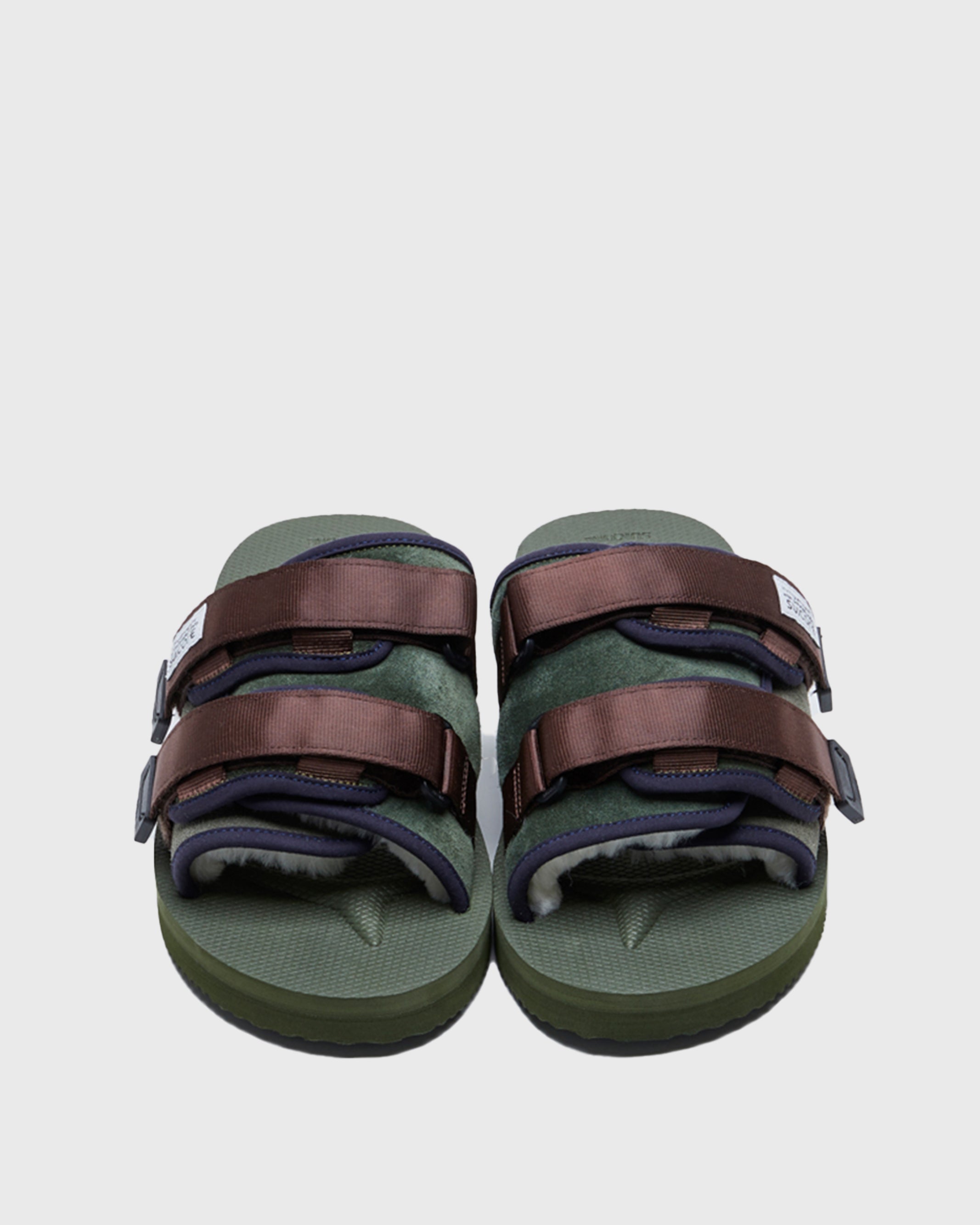 SUICOKE MOTO-Mab suede slides with green midsole and sole, green suede upper and shearling inside with navy piping and brown nylon straps with a logo patch. From Fall/Winter 2021 collection on SUICOKE Official US & Canada Webstore.