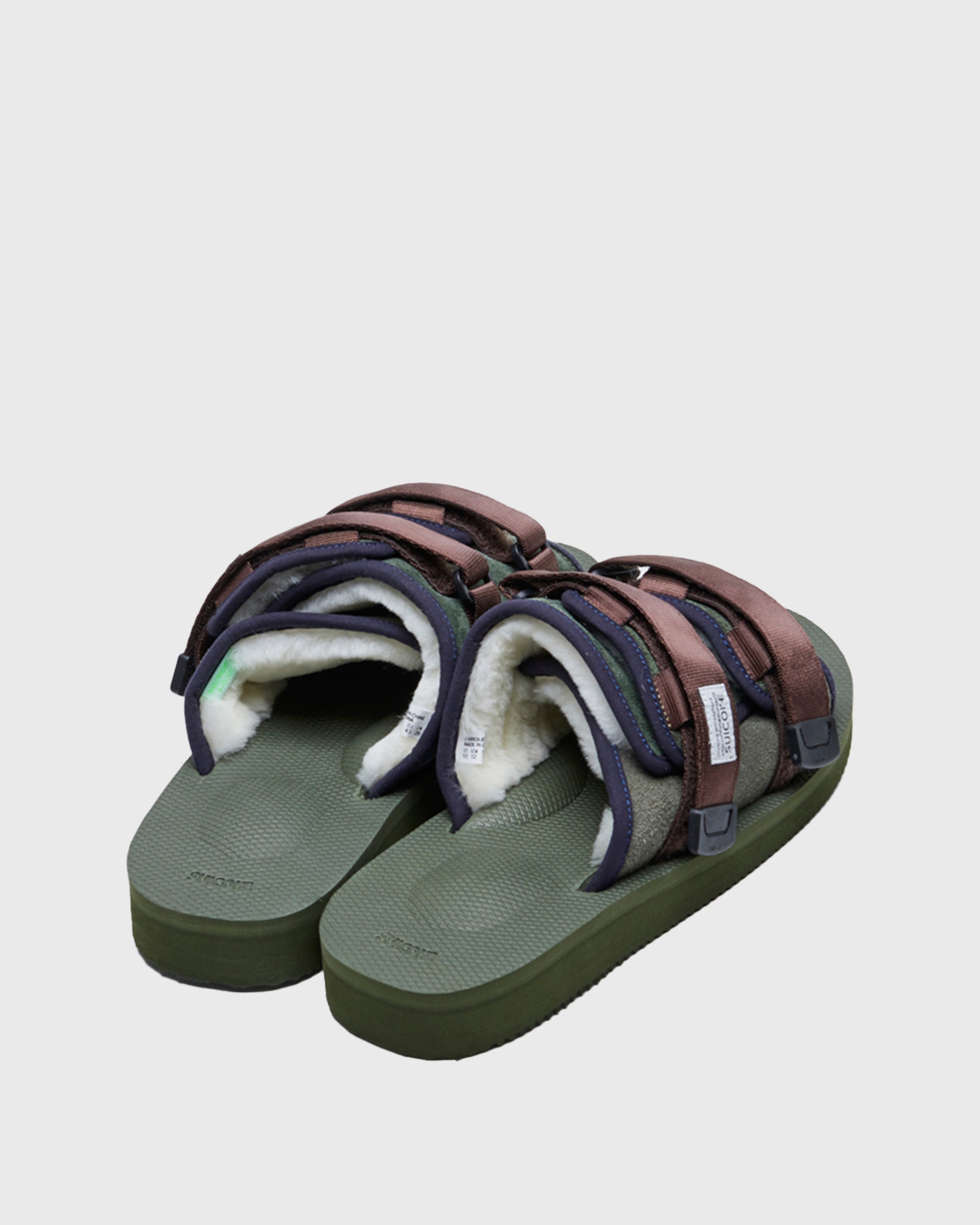 SUICOKE MOTO-Mab suede slides with green midsole and sole, green suede upper and shearling inside with navy piping and brown nylon straps with a logo patch. From Fall/Winter 2021 collection on SUICOKE Official US & Canada Webstore.