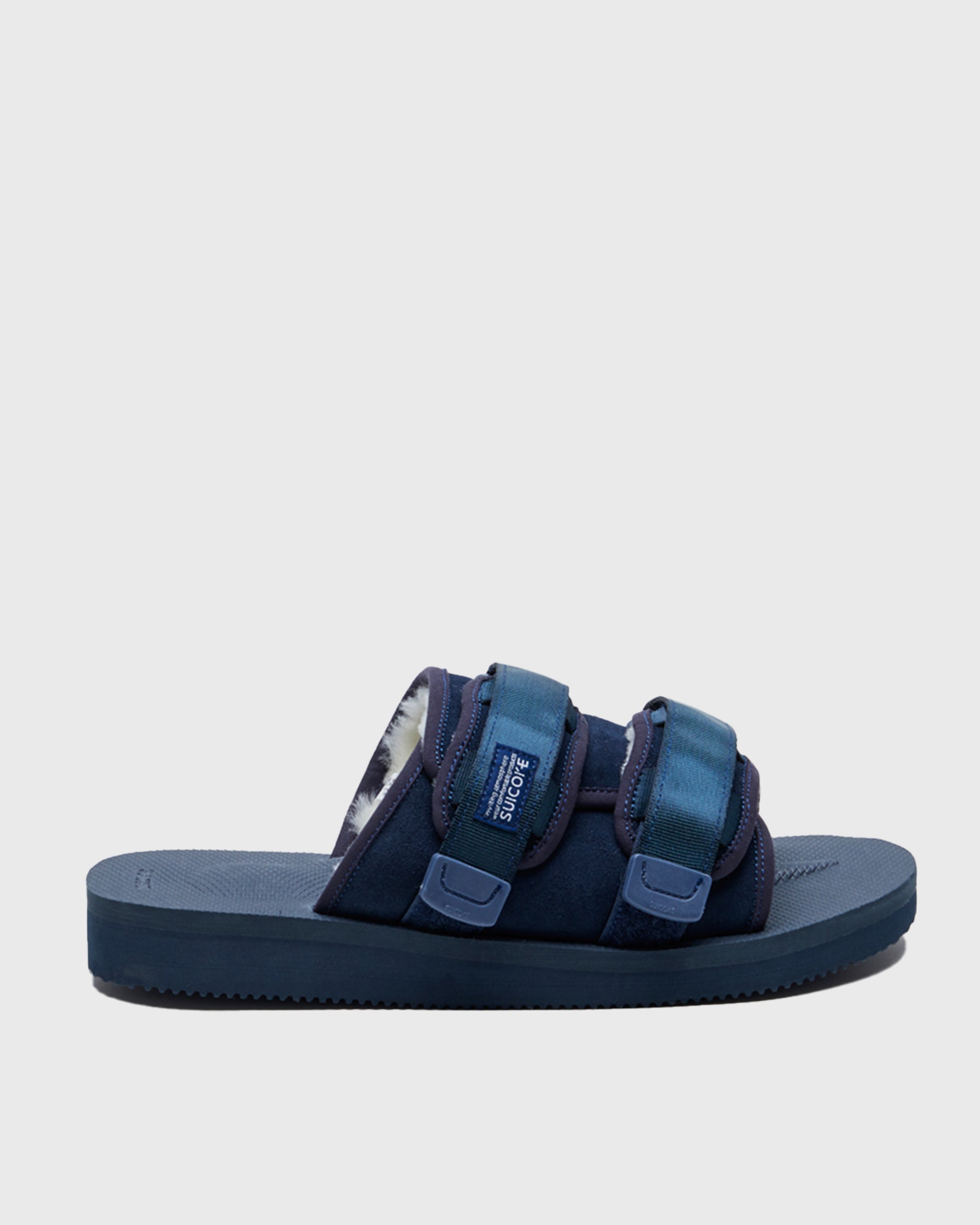 SUICOKE MOTO-Mab suede slides with navy midsole and sole, navy suede upper and shearling inside with navy piping and nylon straps and end tabs, and logo patch. From Fall/Winter 2021 collection on SUICOKE Official US & Canada Webstore.