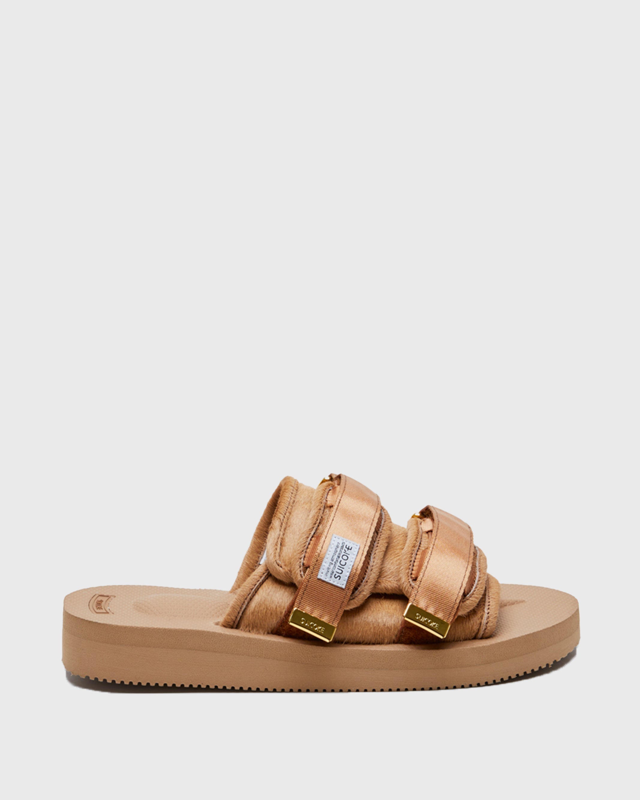 SUICOKE MOTO-Vhl slides with camel colored calf hair upper, camel colored midsole and sole, straps with logo patch and gold logoed tabs. From Fall/Winter 2021 collection on SUICOKE Official US & Canada Webstore.