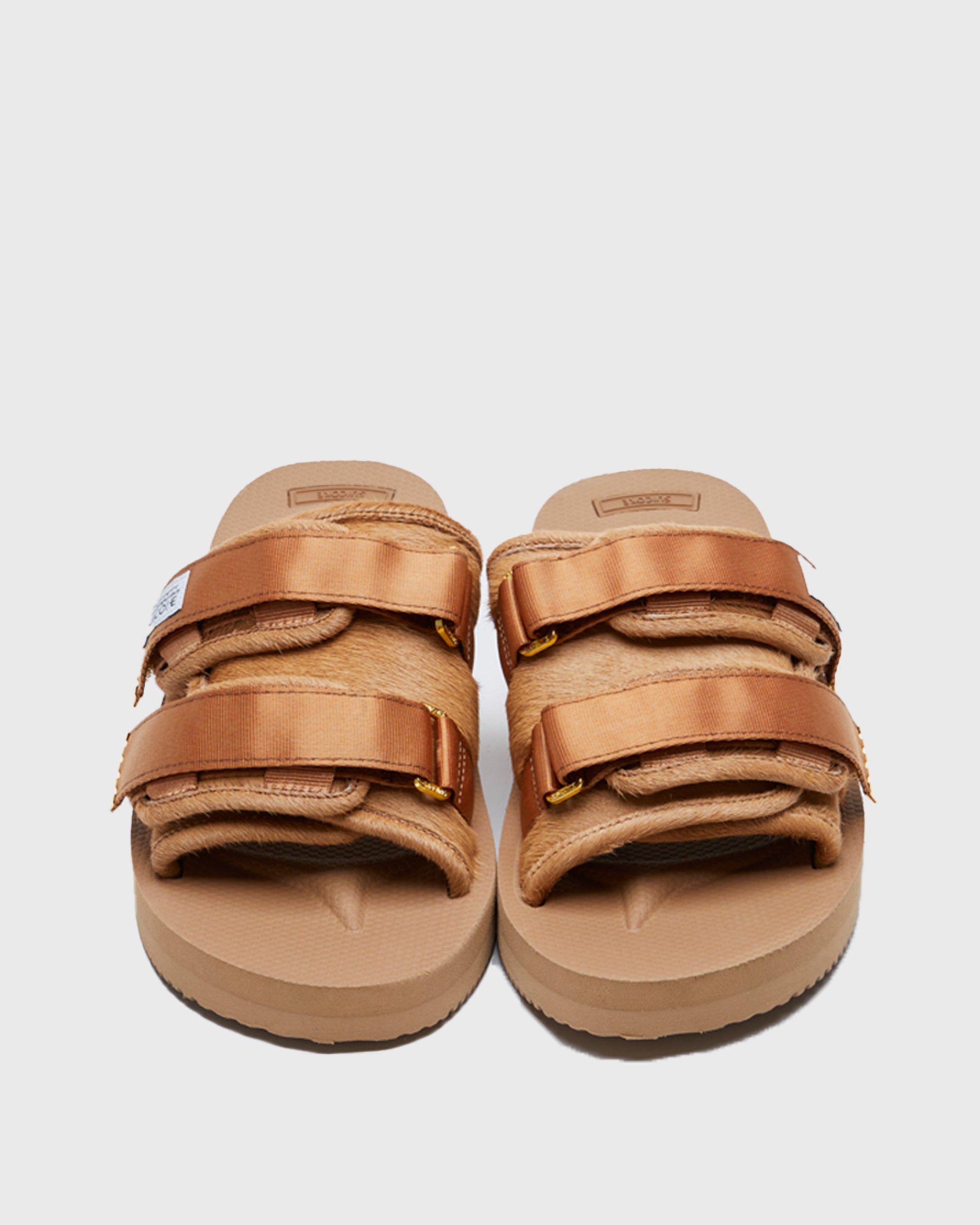 SUICOKE MOTO-Vhl slides with camel colored calf hair upper, camel colored midsole and sole, straps with logo patch and gold logoed tabs. From Fall/Winter 2021 collection on SUICOKE Official US & Canada Webstore.