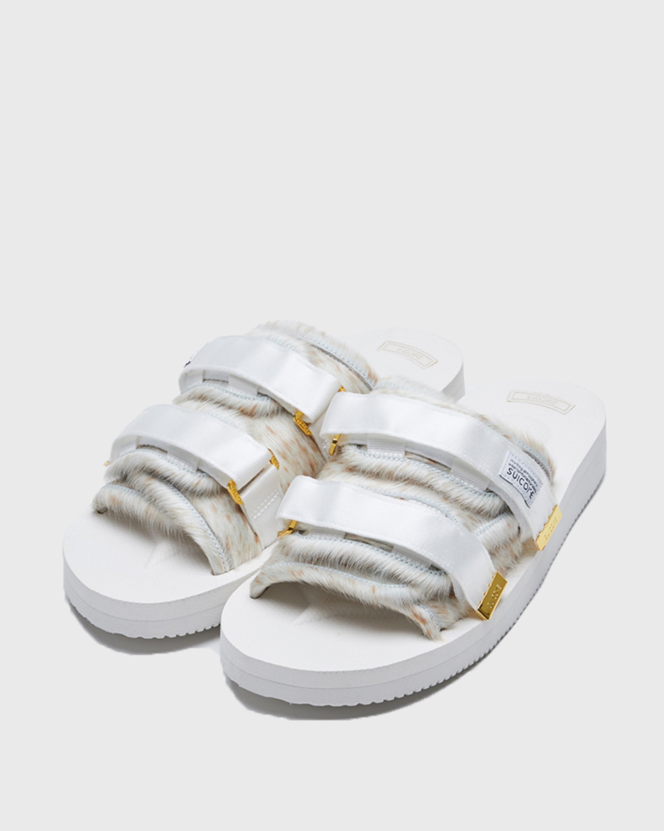 SUICOKE MOTO-Vhl slides with white, brown speckled colored calf hair upper, white midsole and sole, nylon straps with logo patch and gold logoed tabs. From Fall/Winter 2021 collection on SUICOKE Official US & Canada Webstore.