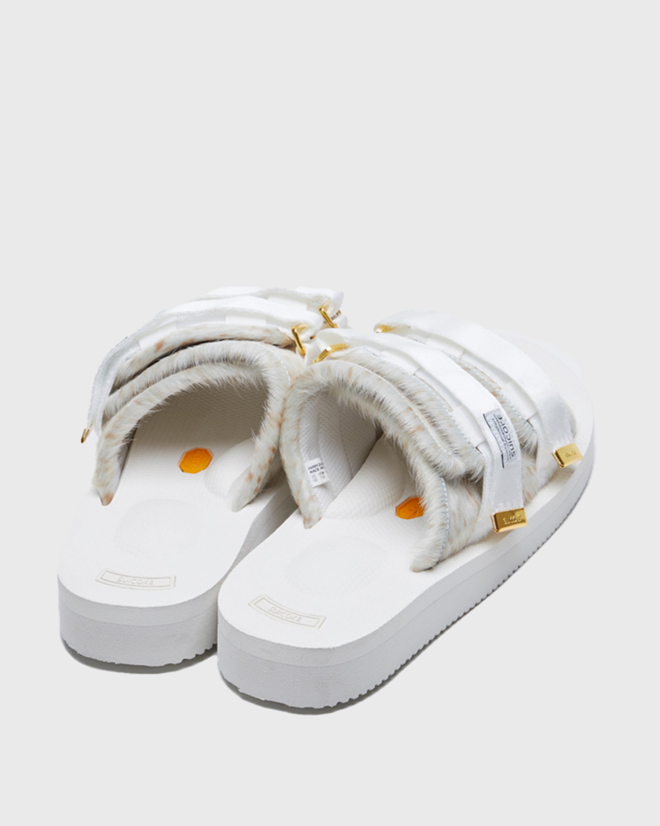 SUICOKE MOTO-Vhl slides with white, brown speckled colored calf hair upper, white midsole and sole, nylon straps with logo patch and gold logoed tabs. From Fall/Winter 2021 collection on SUICOKE Official US & Canada Webstore.