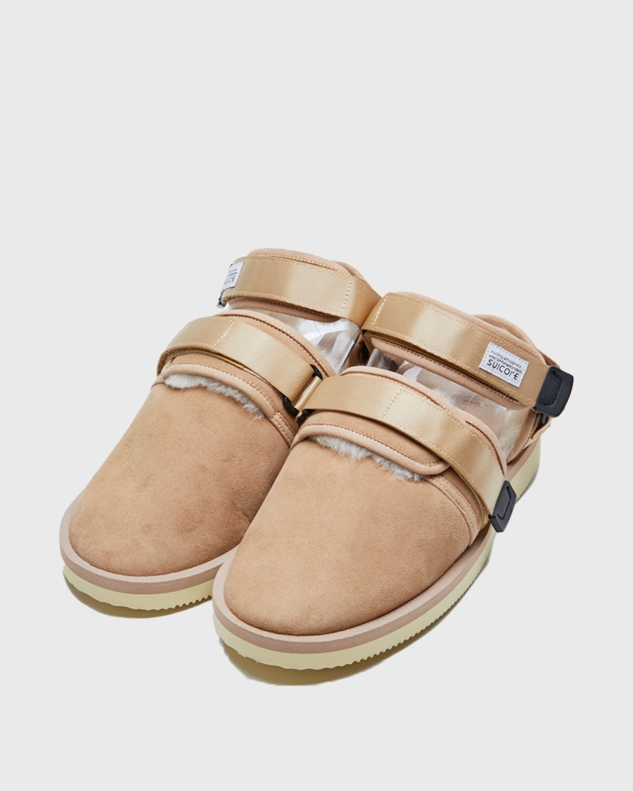 SUICOKE NOTS-M2ab sandals with beige suede upper and midsole and light-yellow sole with shearling inside with beige nylon ankle straps and black tabs with logo patch. Opening between ankle straps and toe upper. From Fall/Winter 2021 collection on SUICOKE Official US & Canada Webstore.