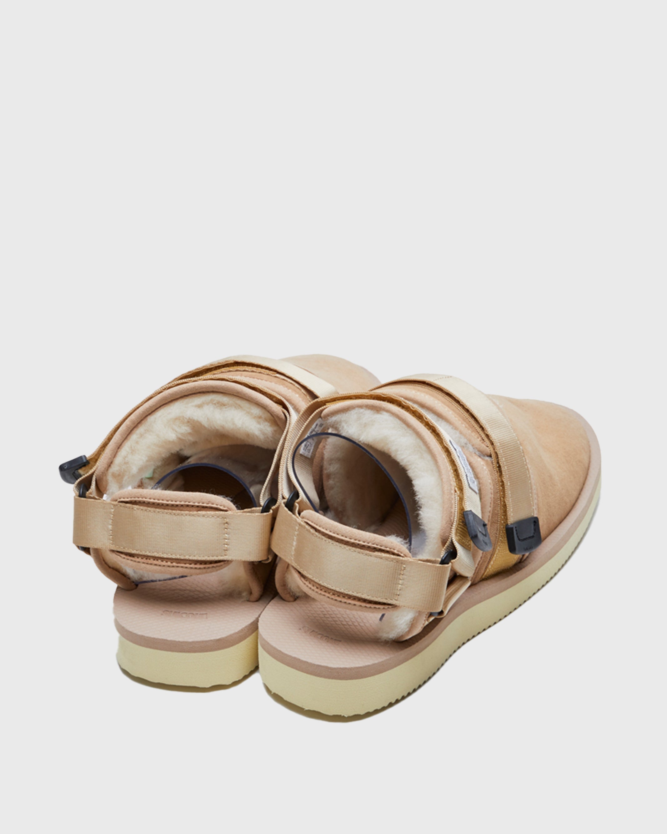 SUICOKE NOTS-M2ab sandals with beige suede upper and midsole and light-yellow sole with shearling inside with beige nylon ankle straps and black tabs with logo patch. Opening between ankle straps and toe upper. From Fall/Winter 2021 collection on SUICOKE Official US & Canada Webstore.