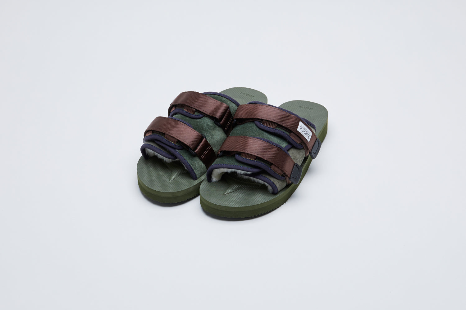 SUICOKE MOTO-Mab suede slides with green midsole and sole, green suede upper and shearling inside with navy piping and brown nylon straps with a logo patch. From Fall/Winter 2021 collection on SUICOKE Official US &amp; Canada Webstore.